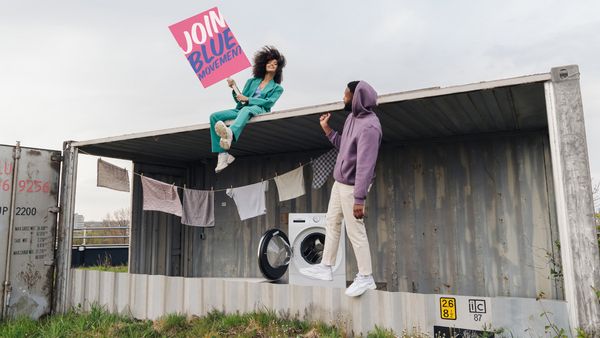 Junge Frau und junger Mann draußen vor einer Wäscheleine und Waschmaschine mit Schriftzug Join Blue Movement.
