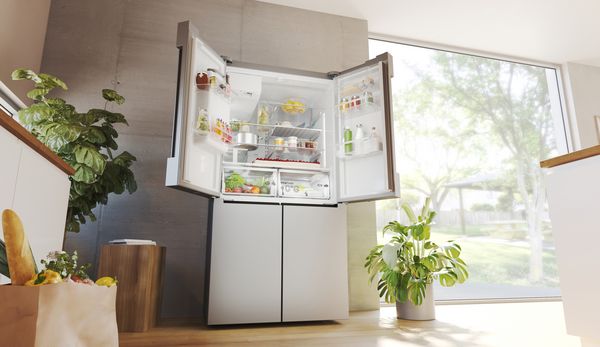 In een heldere witte keuken staat een vrijstaande koelkast, de French Doors helemaal geopend, met zicht op een ruime en goed ingedeelde binnenruimte.