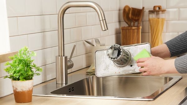 Person washing dishwasher filter over sink