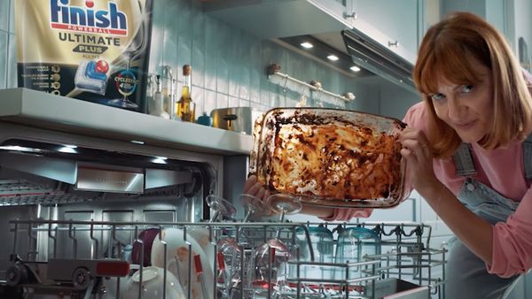 Person putting very dirty bowl in dishwasher with Finish tablets on top of machine