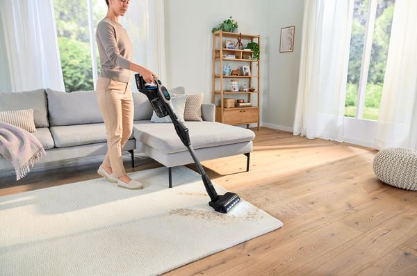 Femme passant l'aspirateur dans un salon avec des meubles et une d&eacute;coration modernes.