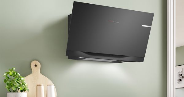 Crni i čelični, kosi zidni aspirator u modernoj kuhinji sa zelenim zidovima.
