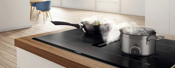 A bright kitchen with a venting hob, extracting the steam from a frying pan and a pot.