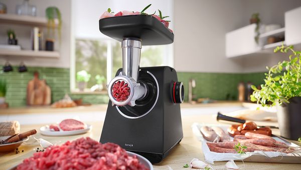 MultiPower Series 4 with meat mincer attachment and plate with minced meat next to plate with sausages on kitchen top.