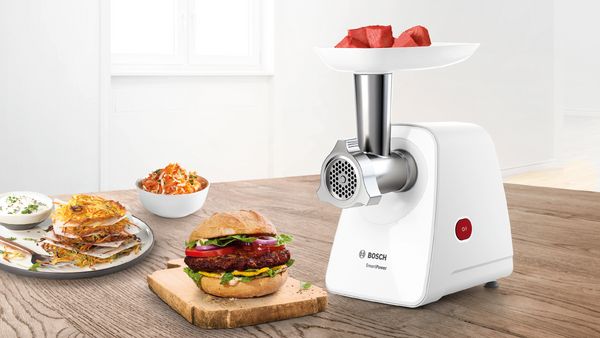 SmartPower meat mincer with meat in tray, next to a burger on board and bowls of dips and salads.
