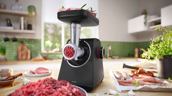  MultiPower Series 4 with meat mincer attachment and plate with minced meat next to plate with sausages on kitchen top.