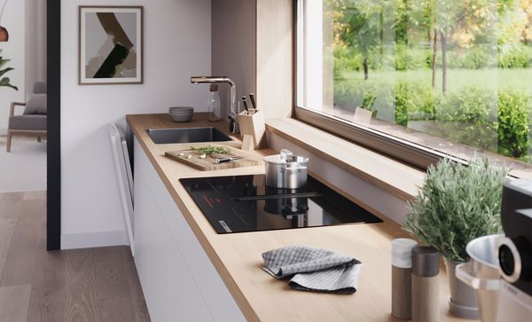 Hoekaanzicht van een keukenopstelling onder een raam met een Bosch-kookplaat met geïntegreerde ventilatiemodule.