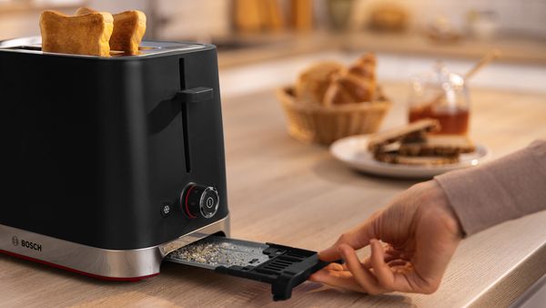 MyMoment black toaster with toasted bread and a hand emptying the crumb tray.