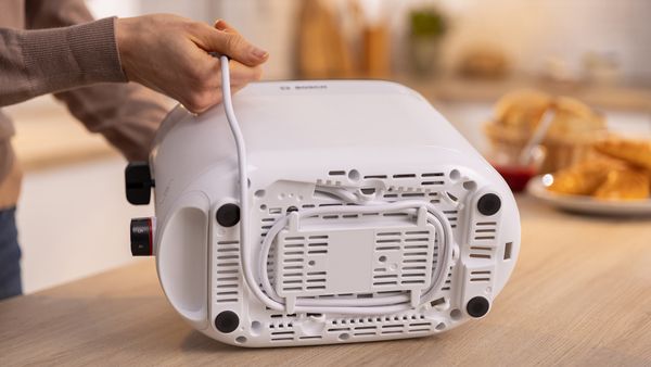 A hand organizing the white MyMoment toaster's cable on a kitchen countertop.
