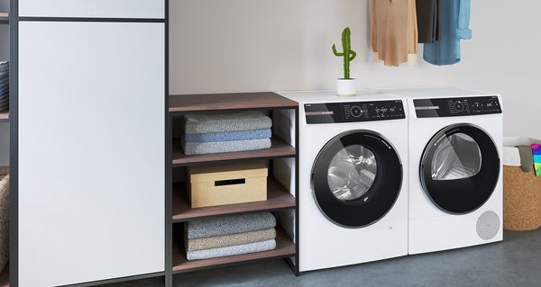 Un lave-linge et un sèche-linge se trouvent entre des étagères et un panier à linge dans une pièce joyeuse.