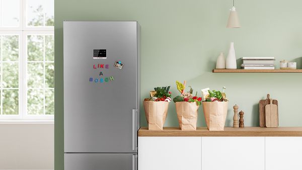 A fridge freezer in a kitchen with grocery bags nearby