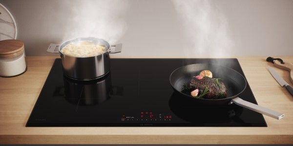 Une grande table à induction avec une poêle dans laquelle cuit un steak.