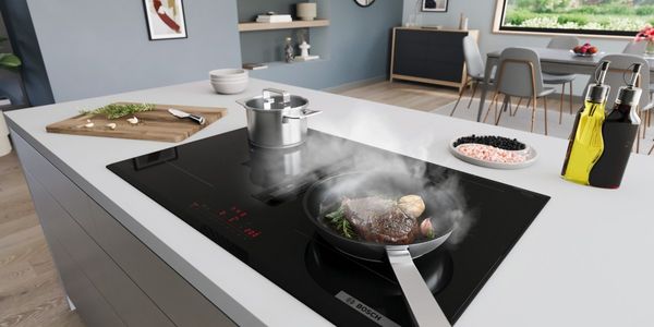 Une casserole et une poêle chaude sur une table à induction qui aspire la vapeur.