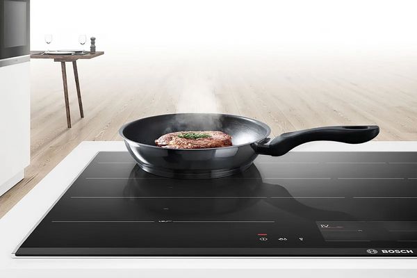 A pot of pasta and a pan with a steak cook on an induction hob.