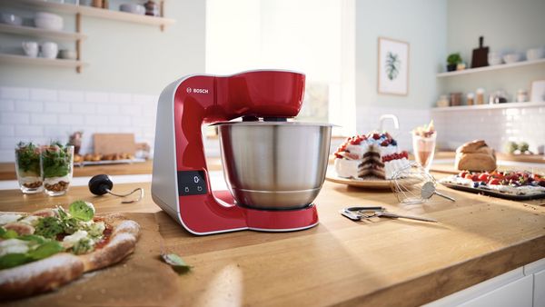 Eine rote Bosch Küchenmaschine Serie 4 steht auf einer Kücheninsel neben Pizza und Kuchen.