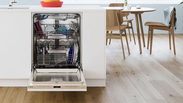 View of an open Bosch dishwasher neatly stacked with plates, cups, glasses and silverware.