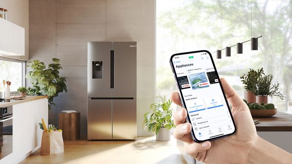 Vooraanzicht van een Multi Door koel-vriescombinatie met snelle ijs- en waterdispenser in een keuken, smartphone met Home Connect-scherm op de voorgrond.