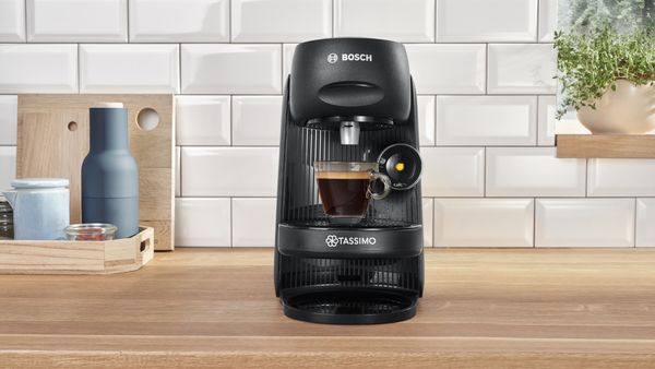 The coffee machine TASSIMO FINESSE on a kitchen worktop with a filled expresso cup.