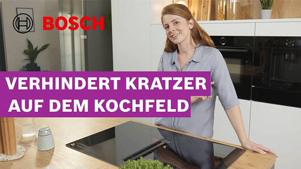 Eine moderne Küche mit einem Kochfeld von Bosch und eine Frau in einem hellgrauen Hemd demonstriert die Kratzfestigkeit des Kochfelds. 