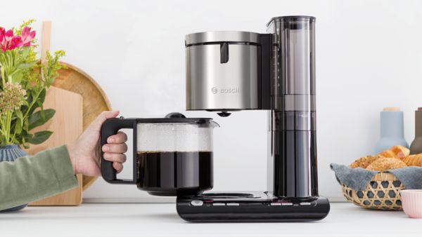 Hand removing MyMoment glass jug and close-up of non-drip device on coffee maker.