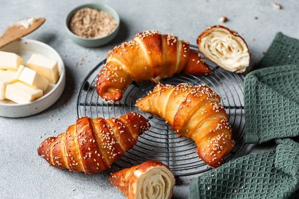 Croissant con semi di sesamo su una griglia di raffreddamento, con burro e zucchero di canna sul tavolo