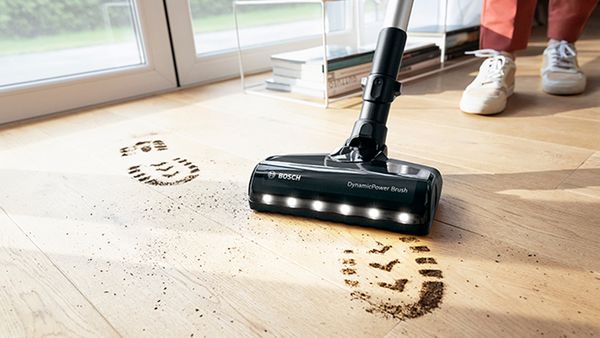 A person using a vacuum cleaner to clean the dearty foorprints on the floor.