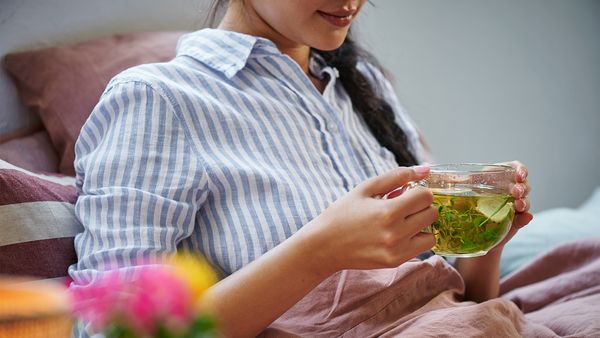 Eine Frau in blau-weiß gestreifter Bluse hält eine Glastasse mit Kräutertee in den Händen.