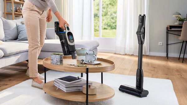 Femme passant l'aspirateur sur une table avec l'appareil portatif Unlimited tandis que le tube et l'embout se trouvent à côté grâce à la fonction Quick Stand.