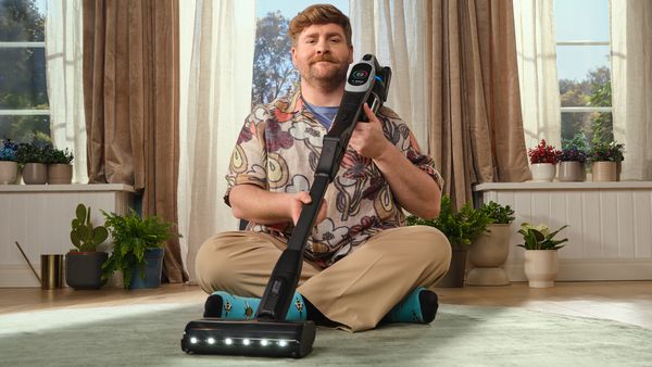 Homme assis les jambes croisées sur un tapis, l'aspirateur Unlimited sur ses genoux, contre son épaule.