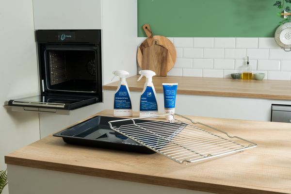 Ett rengöringskit för ugnar från Bosch som innehåller en flaska rengöringsgel-spray, en flaska avfettningsmedel och en borste. Produkterna står framför ett skinande rent ugnsgaller.