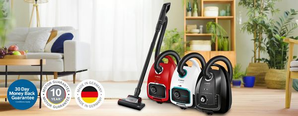 Three bagged vacuum cleaners in black, red and silver, forming a triangle on an off-white rug in a living room with hardwood flooring