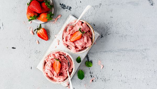 Dve skodelici jagodne kreme s svežimi rezinami jagod, postreženi na površini z rahlo teksturo, z majhno skledo celih jagod v bližini.