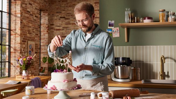 Ein Mann mittleren Alters verziert eine zweistufige selbst gebackene Hochzeitstorte.