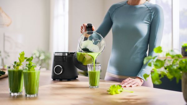 Frau gießt grünen Smoothie aus dem VitaPower Serie 6 Mixbehälter in ein Glas.