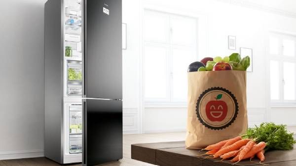 Un meuble de cuisine présente un réfrigérateur-congélateur bien rempli aux portes ouvertes sur le côté droit. À gauche, un lave-vaisselle est intégré dans le meuble de cuisine.