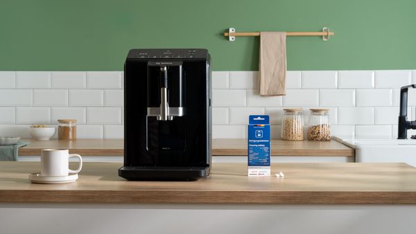 Une cuisine blanche avec une machine à expresso Bosch. Au premier plan, un emballage de filtre à eau Brita est posé à côté de plusieurs tasses de café et de latte. 