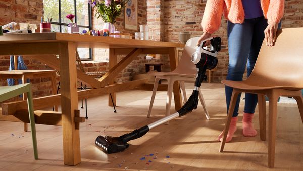 Eine Person saugt Papierschnipsel unter einem Tisch mit dem Unlimited 7 Akku-Staubsauger von Bosch weg.