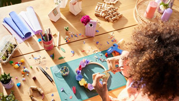 Es ist ein Tisch mit verschiedenen Upcycling-Bastelmaterialien zu sehen sowie eine Person, die einen Blütenkranz bastelt.