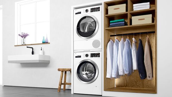 Eine Bosch-Waschmaschine und ein Bosch-Wäschetrockner wurden gestapelt und in einen Wäscheschrank integriert, in dem Hemden und Sakkos zu sehen sind.