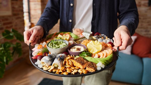 Eine Person trägt ein Tablett mit einem Seacuterie Board, auf dem verschiedene Aufschnitte, Rohkost sowie Dips zu sehen sind.