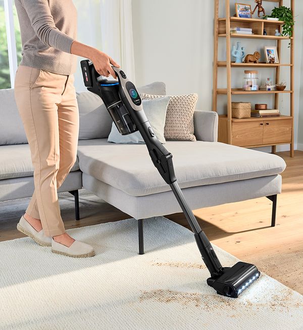 Woman vacuuming up dirt along the edge of the kitchen cabinet with the Unlimited.