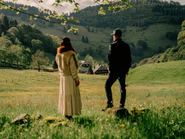 A portrait of Katharina and Helmut looking back at the Black Forest House from high up on a hillside