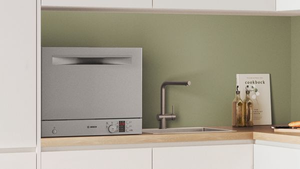 A countertop dishwasher with an open door and a full rack on a kitchen worktop.