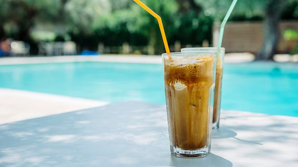 Two glasses of iced coffee with straws on a table beside a swimming pool, showcasing a refreshing summer vibe.