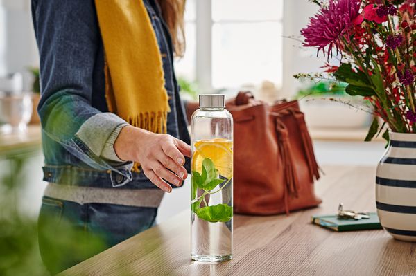 Frau greift nach Wasserflasche voller Infused-Water mit Kräutern und Zitrone.