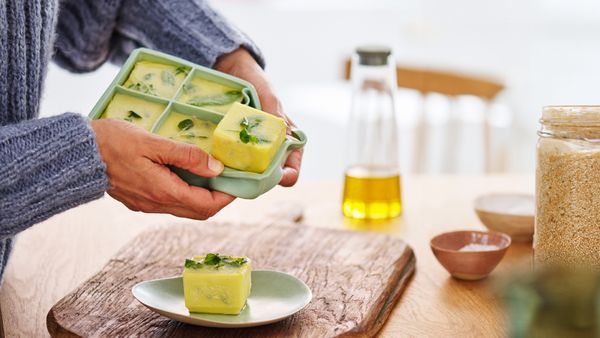 Eine Person gibt selbstgemachte Kräuterbutter aus einer Eiswürfelform auf einen Teller.