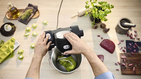 Ein Mann knetet Teig mit Basilikum in der Bosch Küchenmaschine Serie 6 und bereitet frische Ravioli zu.