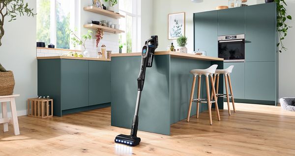 Aspirapolvere verticale moderni appoggiato in una cucina luminosa e minimalista con mobili verdi.