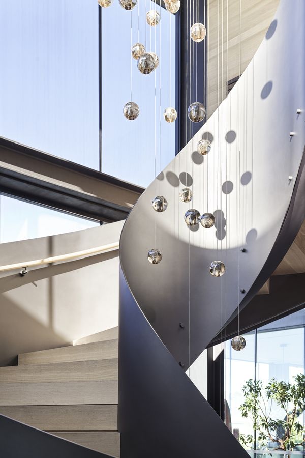 A bright spiral staircase with modern lighting hanging down the center