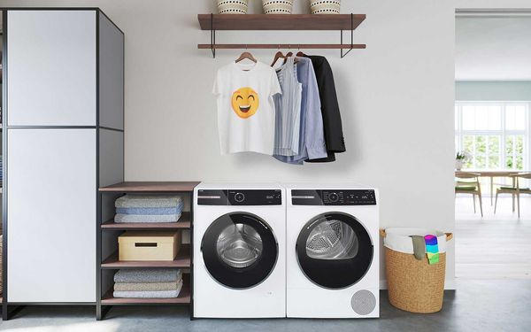 Lave-linge et sèche-linge Série 8 installés l'un à côté de l'autre. Les vêtements sans plis sont suspendus sur des cintres au-dessus. Un T-shirt avec un smiley qui rit.